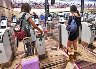 Passengers scan their passports at automated immigration gates at the newly-opened Changi International Airport's Terminal 4 in Singapore on October 31, 2017. 
Singapore's newly-opened automated Changi International airport Terminal 4 began full operations on October 31. The cutting edge terminal, which is half the size of Terminal 3 at 225,000 square meters, makes it Changi Airport's smallest terminal. / AFP PHOTO / ROSLAN RAHMAN