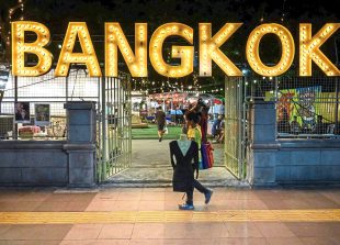 A woman carries clothes as she walks in front of the entrance of Artbox Thailand Night Market in Bangkok on August 19, 2019. (Photo by Mladen ANTONOV / AFP)