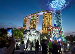 Tourists take pictures in front of two majestic life-size statues of Optimus Prime and Optimus Primal at Gardens By The Bay in Singapore, Saturday, March 18, 2023. (AP Photo/Yeen Ling Chong)